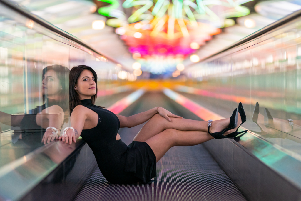 Shei sitting on an airport moving walkway under colorful neon lights.