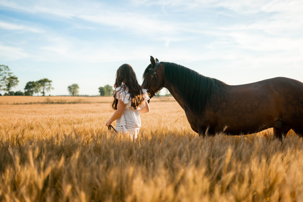 Michaela with a horse in a golden wheat field.