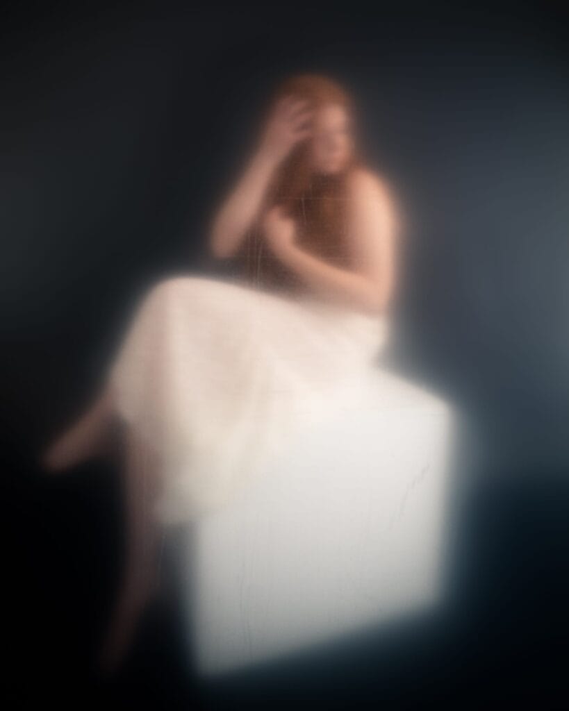 Elizabeth raises a hand to her forehead in a hazy portrait through translucent material.