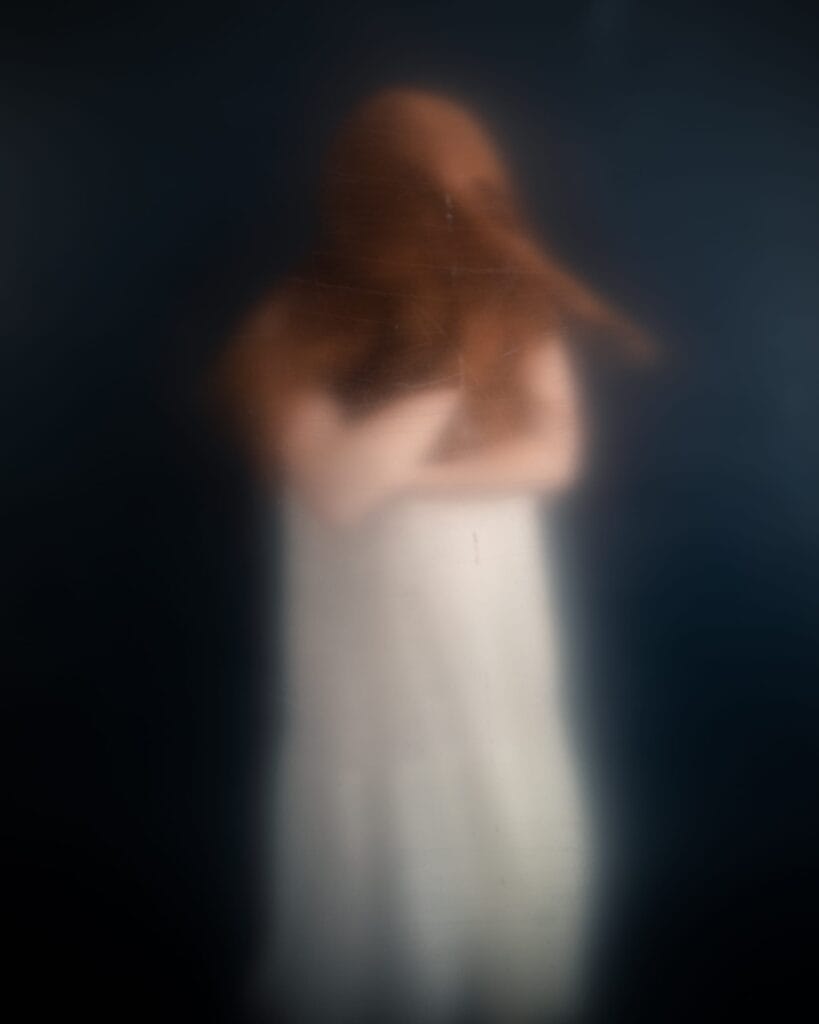 Elizabeth’s red hair sweeps across her face in a heavily blurred studio portrait.