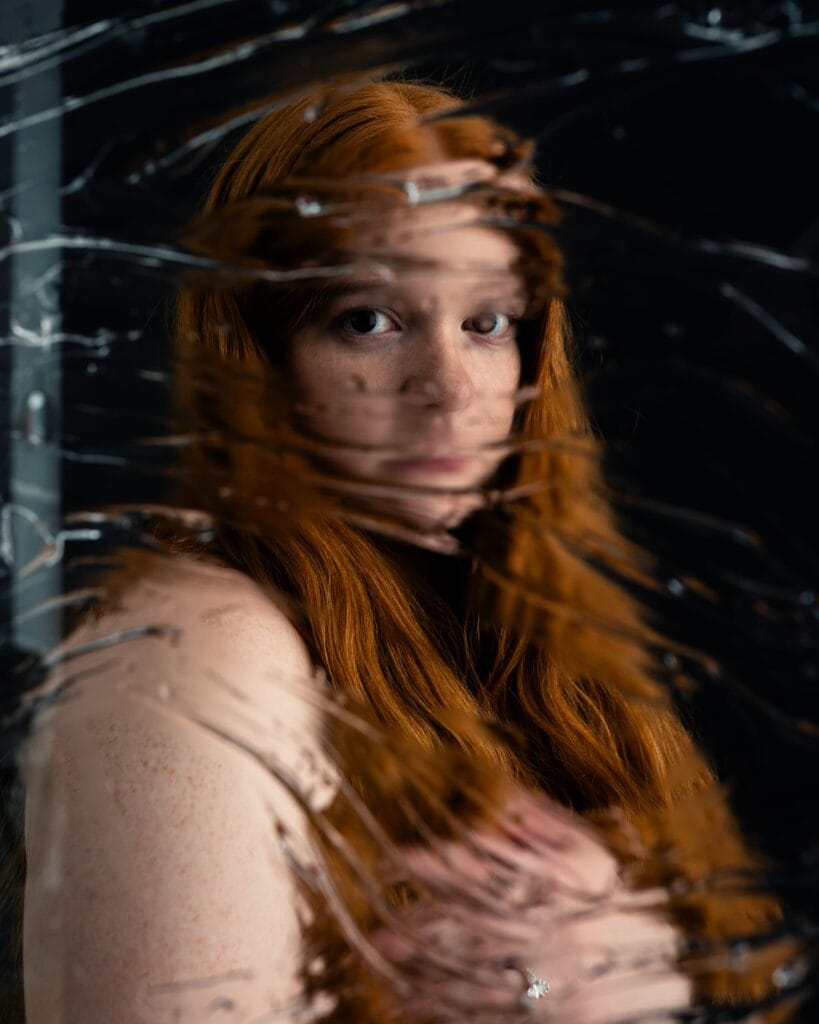 Elizabeth looks toward the camera through streaks of distortion, with her eyes and red hair visible.