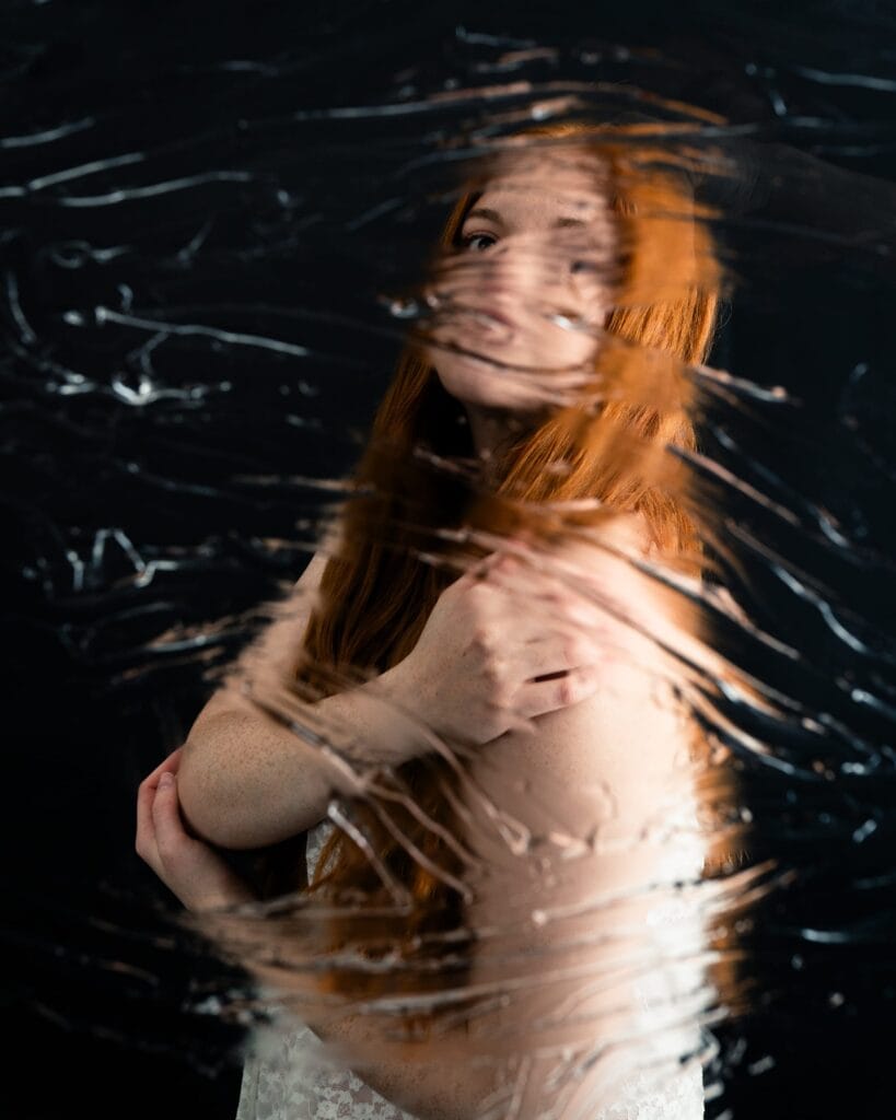 Elizabeth folds her arms across her shoulders behind a rippled, distorting surface.