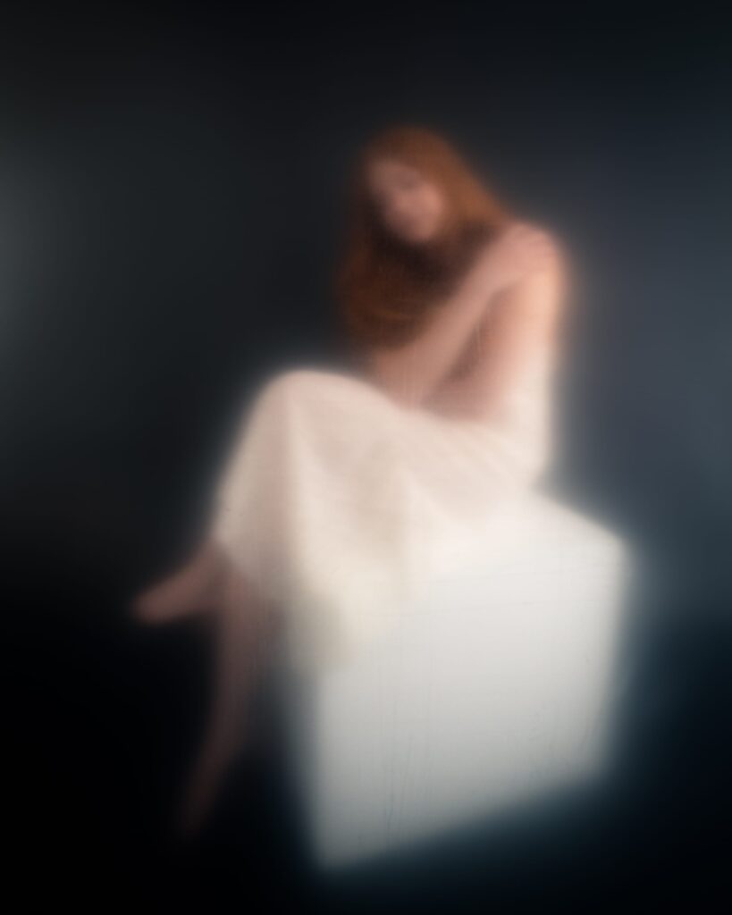 Elizabeth seated in a white dress, her figure softly blurred by material in front of the lens.