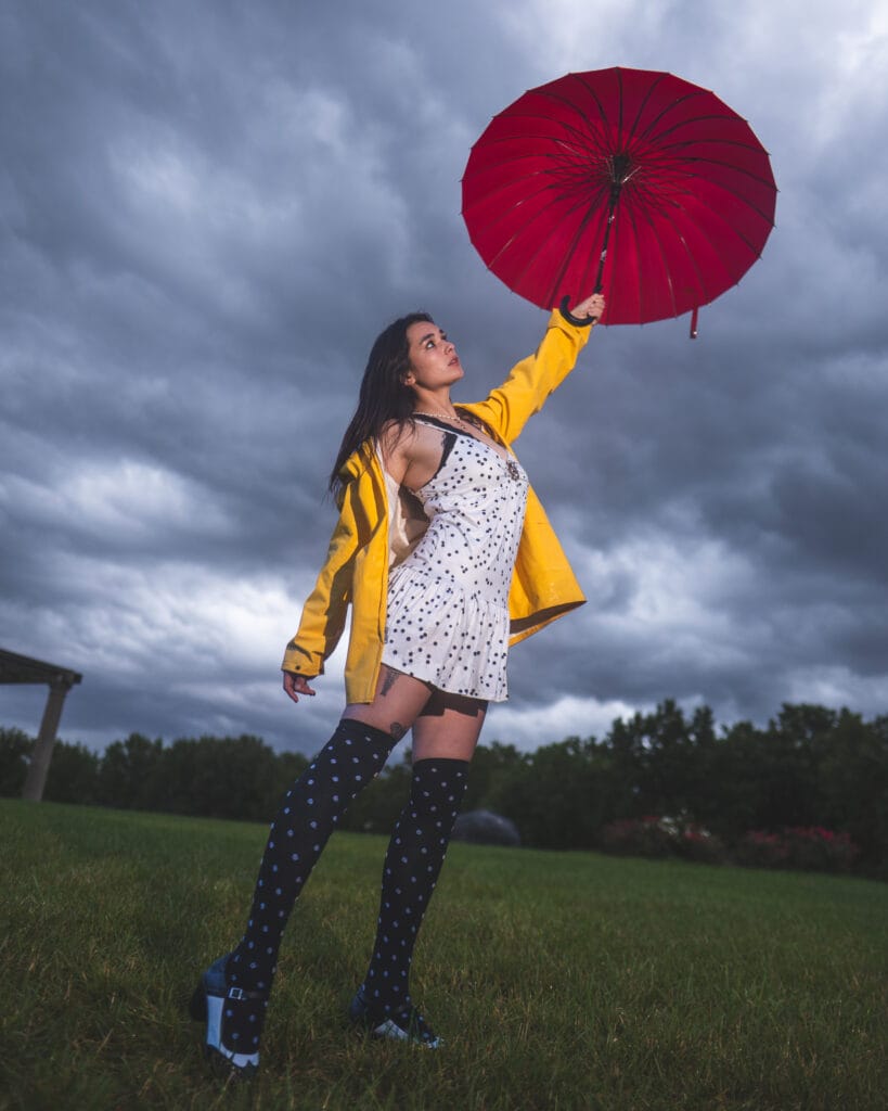 Reese raises a red umbrella overhead in her yellow raincoat.