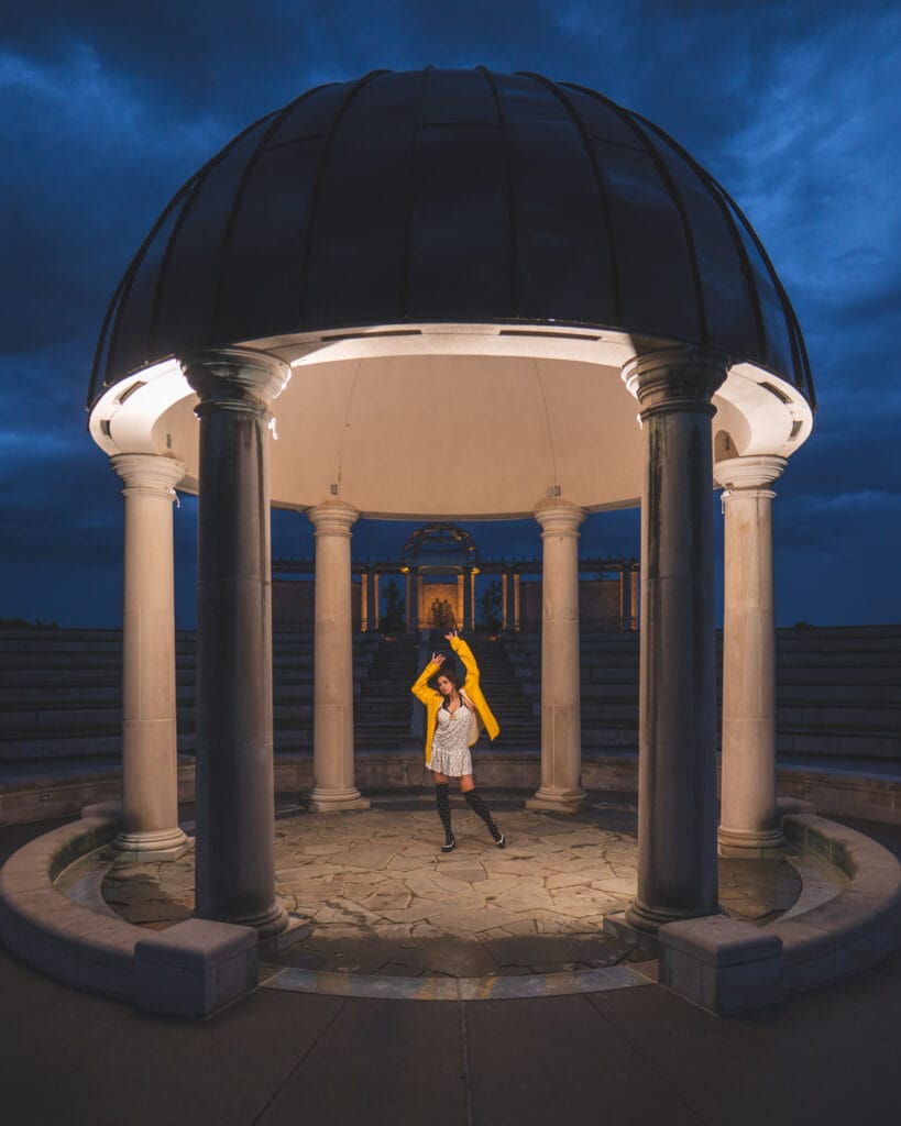 Reese stands inside an illuminated stone pavilion beneath a deep blue evening sky.