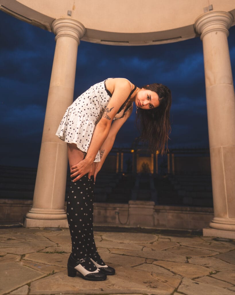 Reese bends sideways with her hair hanging down inside the stone pavilion.