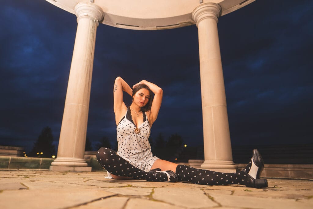 Reese sits beneath pavilion columns with her arms raised above her head.