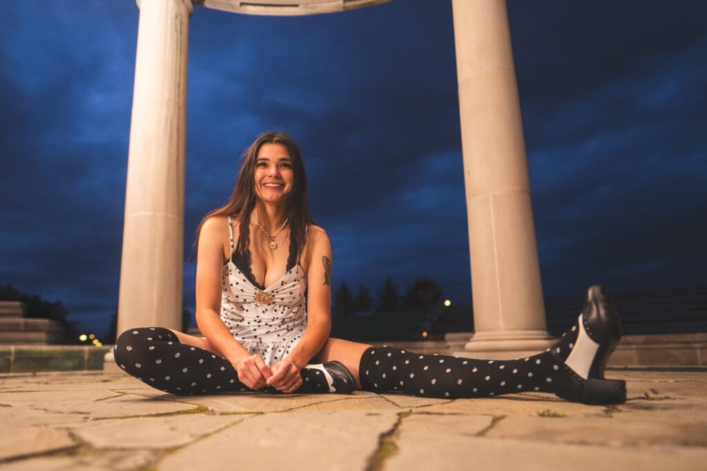 Reese smiles while sitting on the stone floor between pavilion columns.