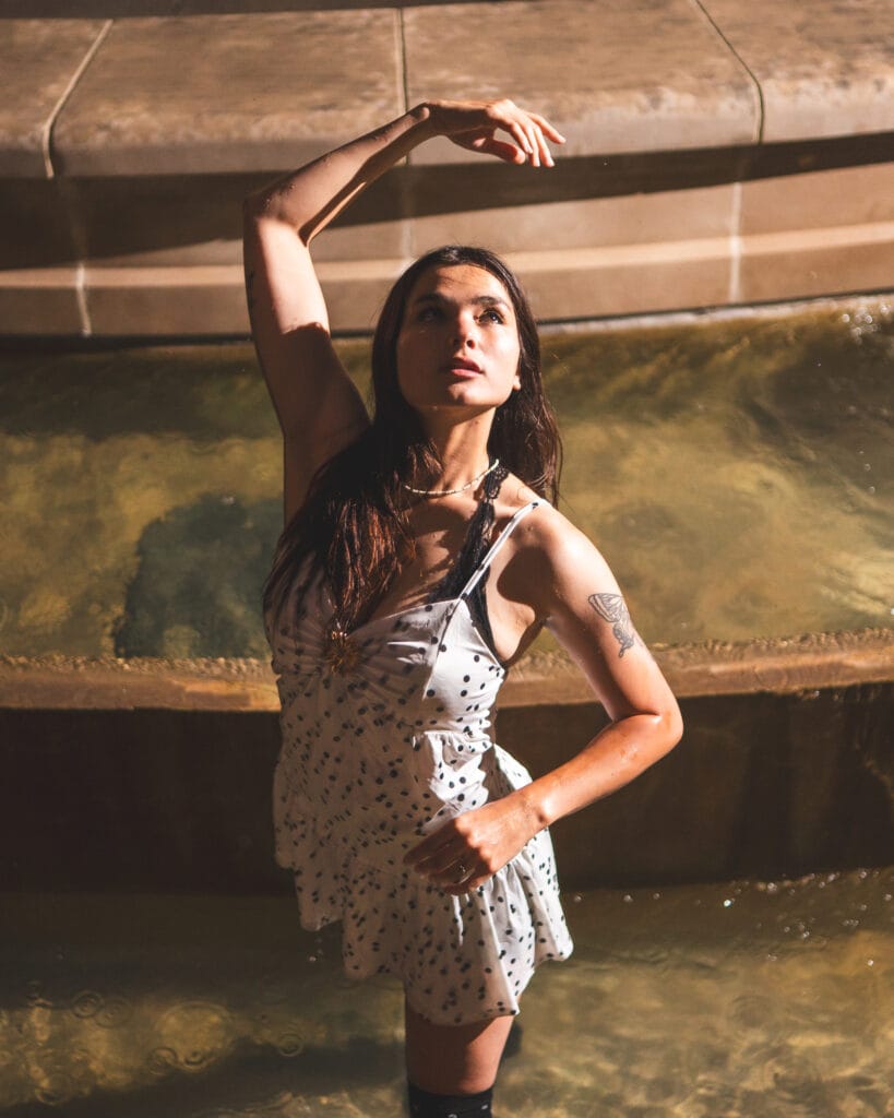 Reese poses in a shallow fountain with one arm arched overhead.