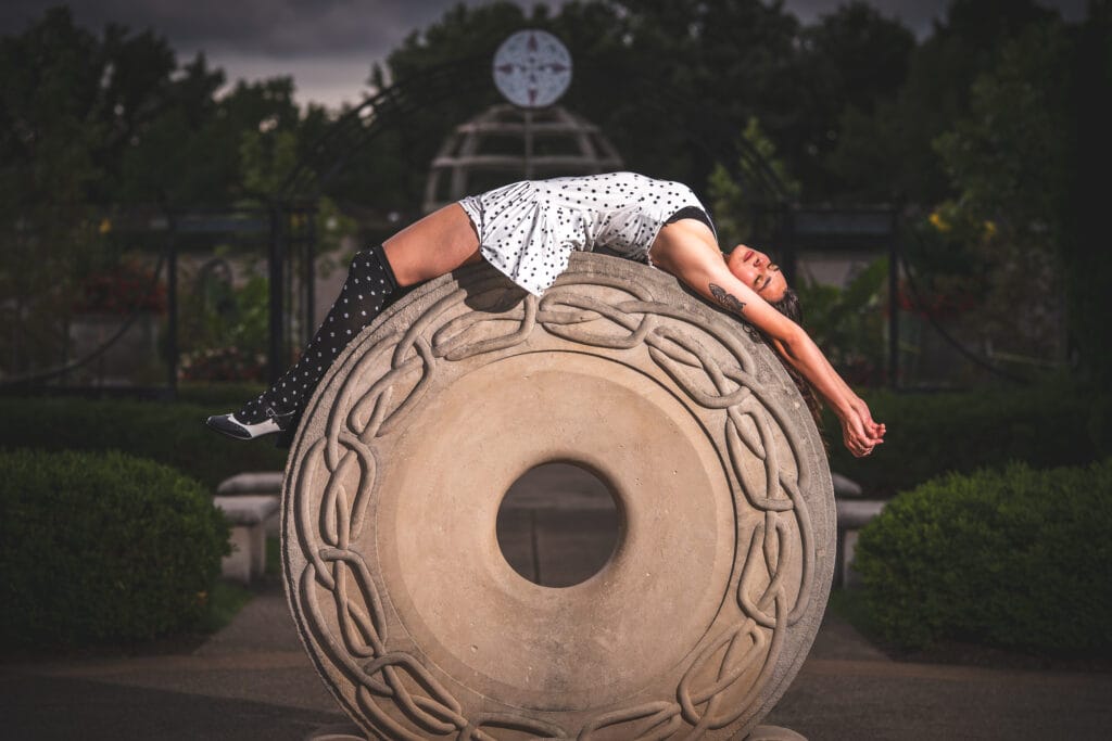 Reese drapes herself over a carved stone sculpture with her arms hanging down.