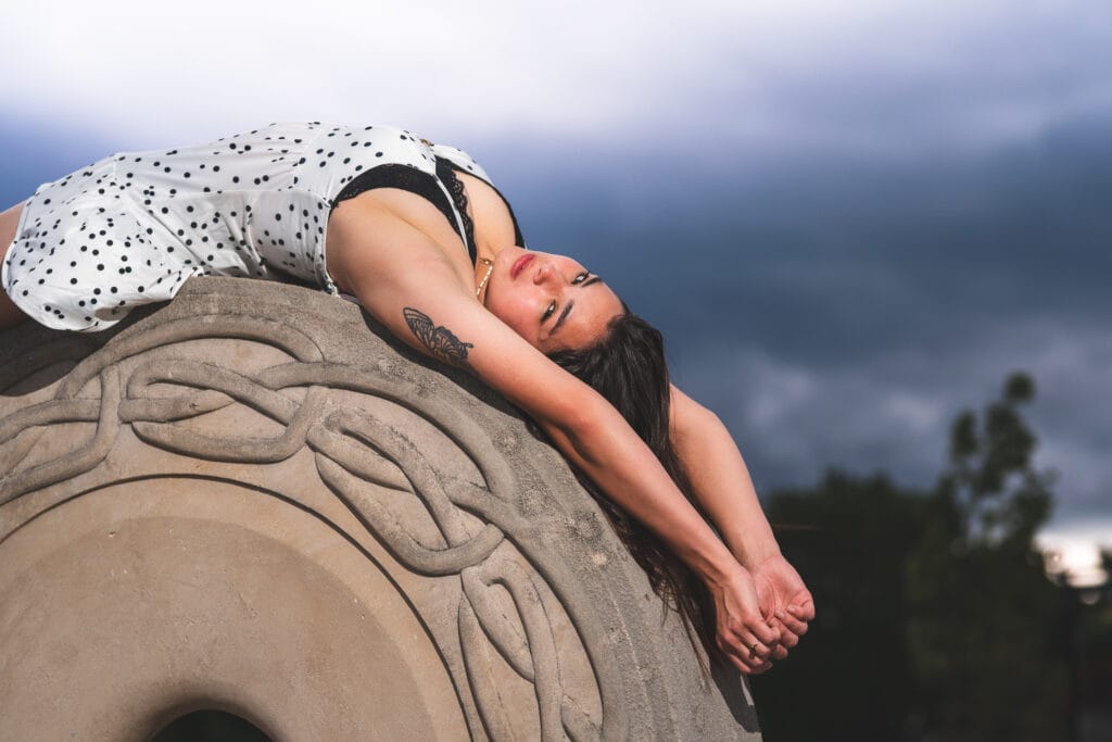 Reese reclines across a carved stone sculpture beneath a dark stormy sky.