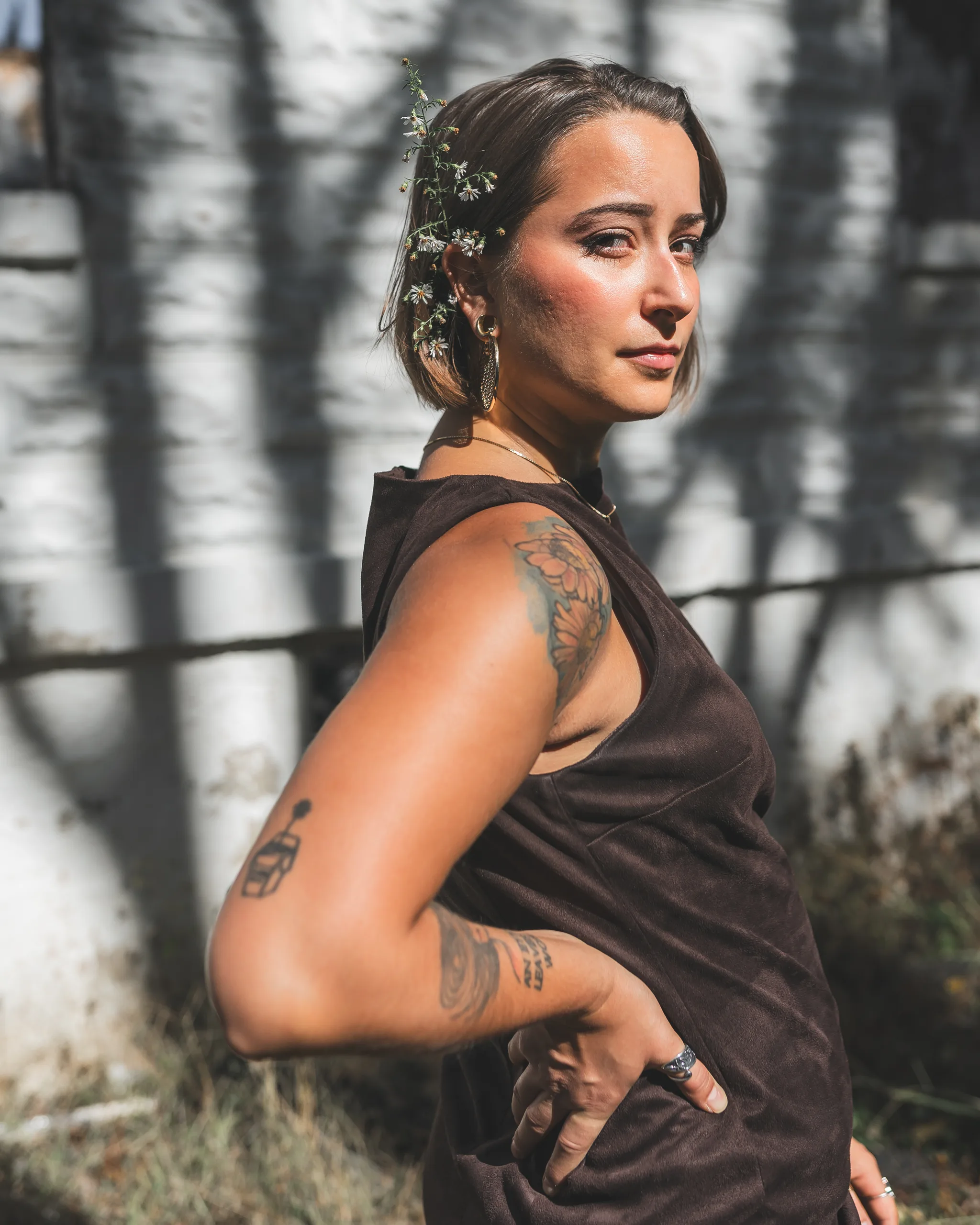 Kaitlyn looks over her shoulder in the brown dress as sunlight and shadows cross the church wall behind her.
