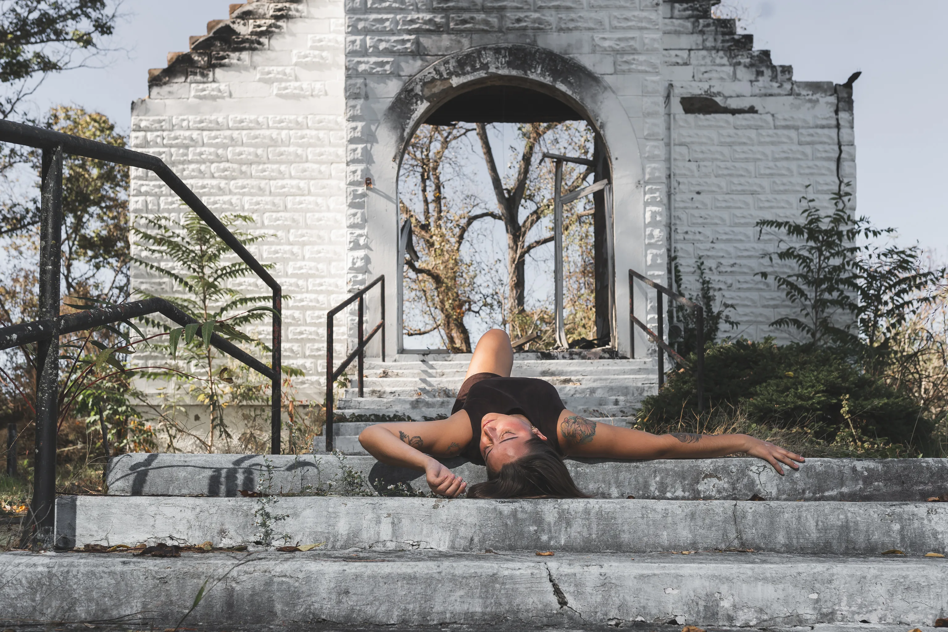 Kaitlyn lies playfully across the church steps in her brown dress, with one arm extended.