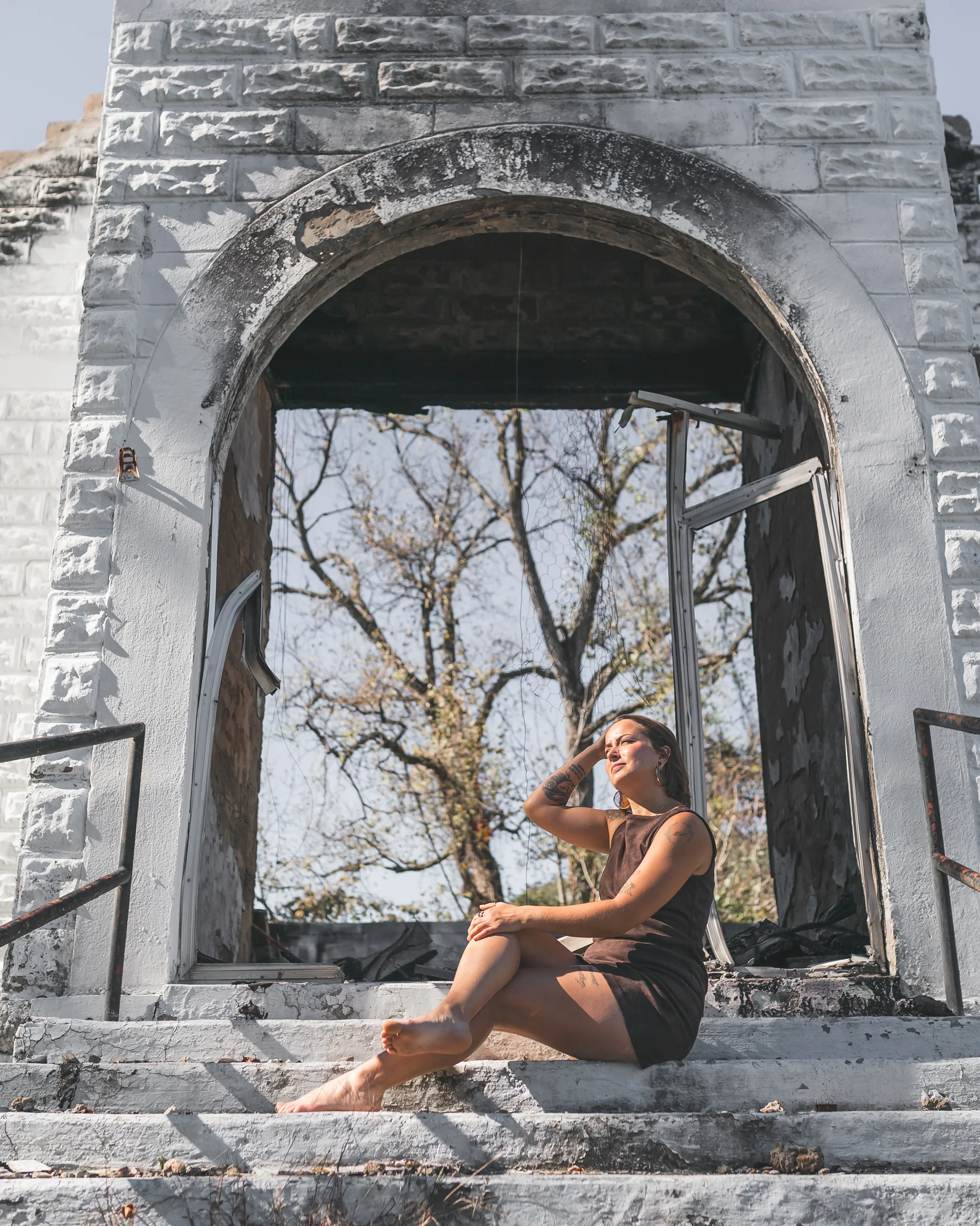 Kaitlyn sits on the church steps beneath the large empty arched doorway in her brown dress.