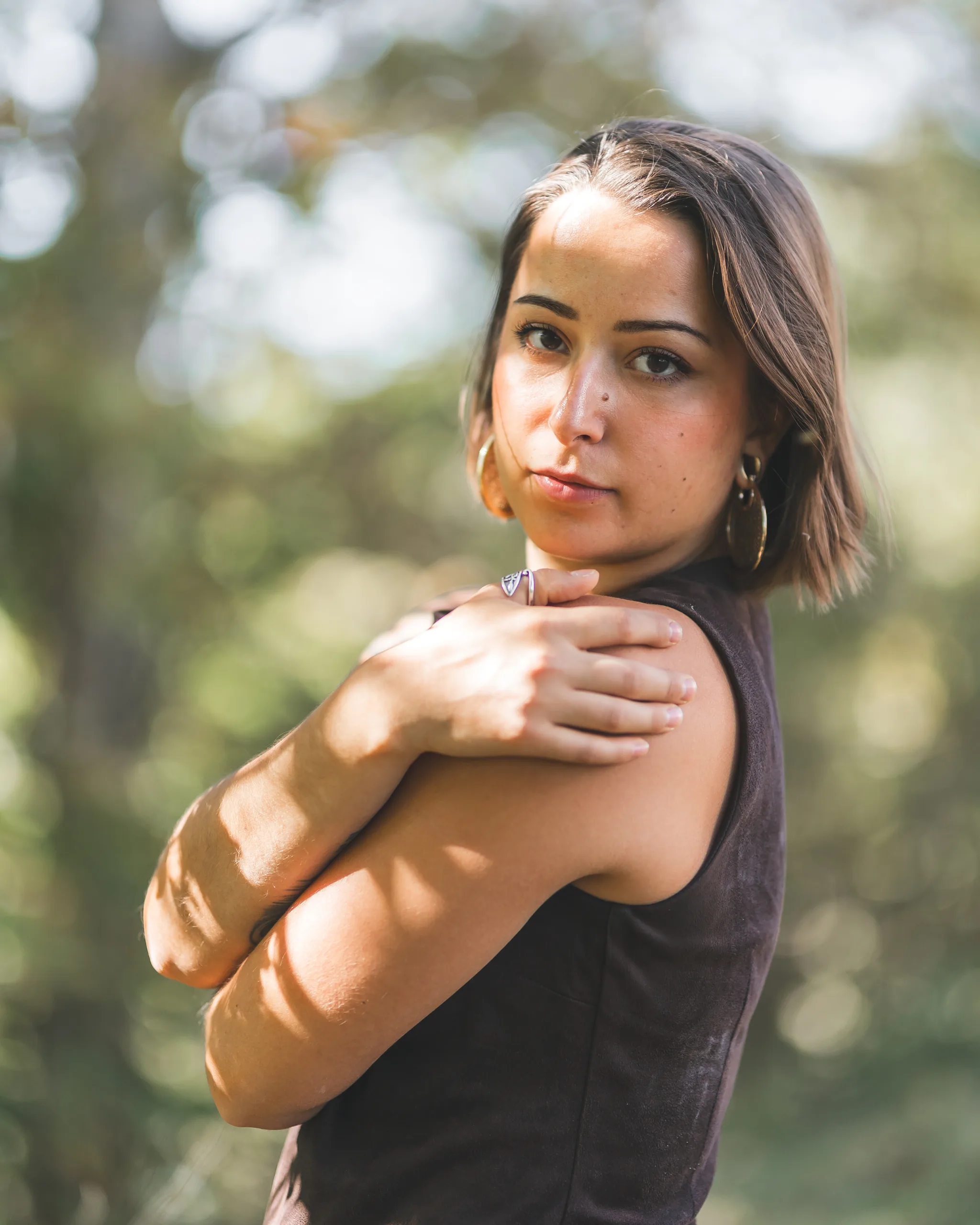 Kaitlyn looks toward the camera beneath the trees, with one hand resting on her shoulder.