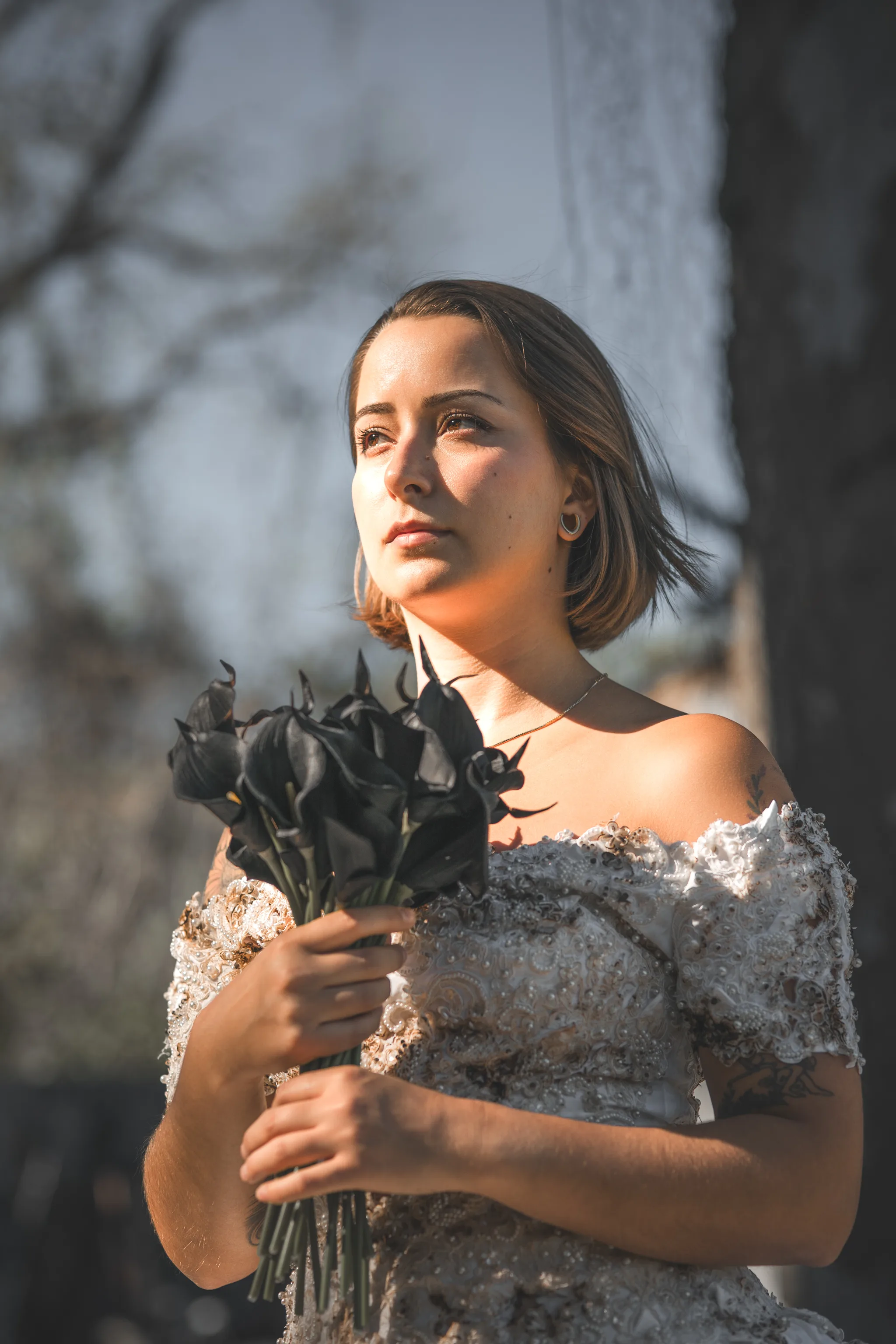 Warm sunlight falls across Kaitlyn’s face as she holds black flowers in her distressed wedding dress.